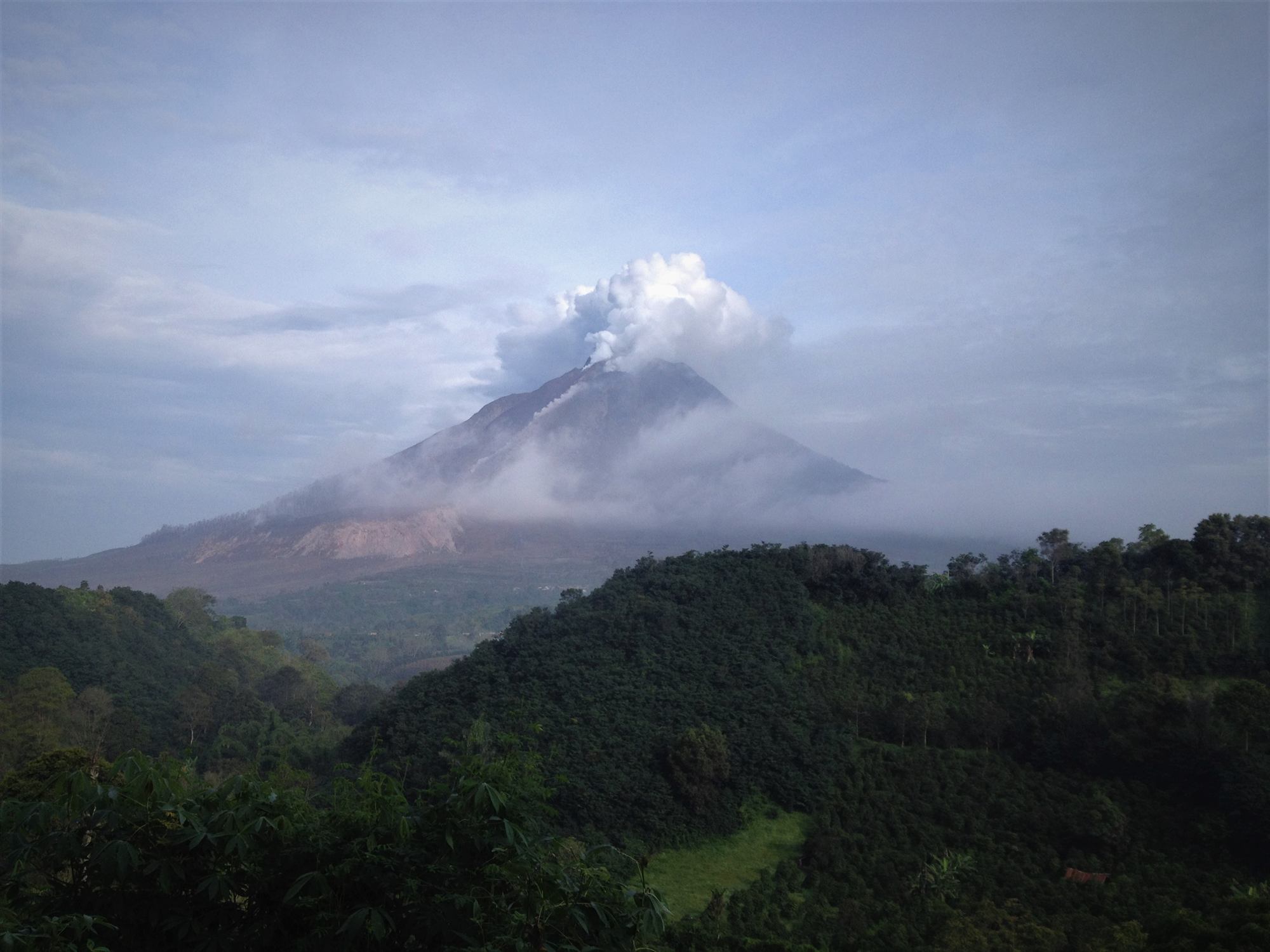 Gunung Sinabung menjulang di antara perbukitan hijau Tanah Karo